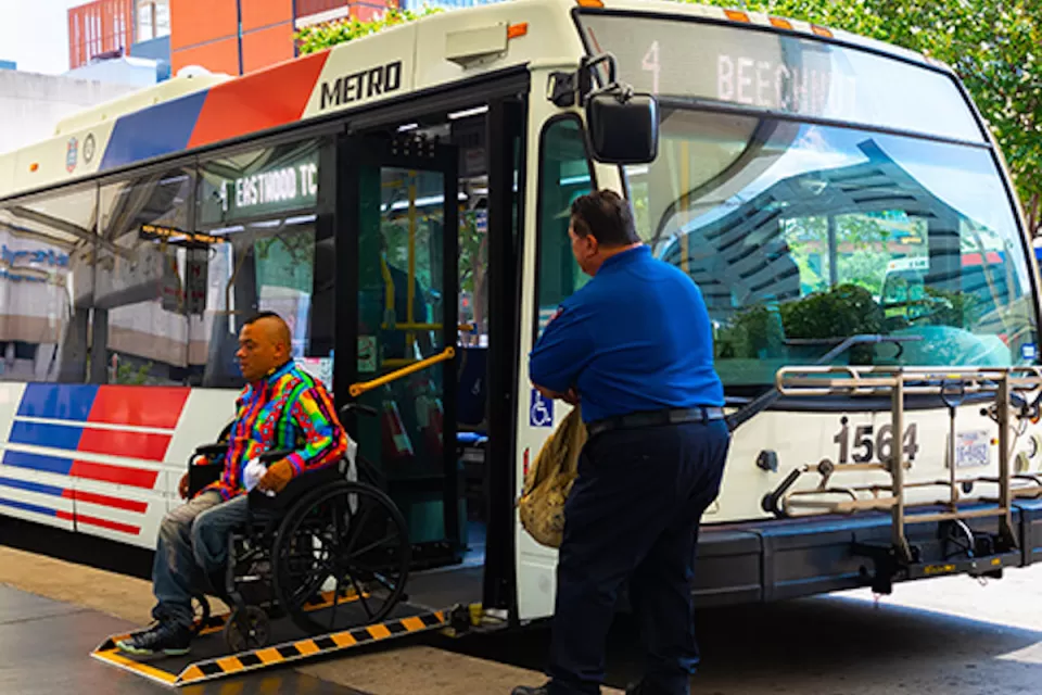 Man in wheelchair exiting public bus on ramp while operator waits outside in Houston, Texas.